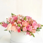 Beautiful flower arrangement, including various shades of pink roses, pink hydrangeas, pink snapdragons in a white round box