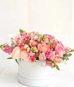 beautiful flower arrangement, including various shades of pink roses, pink hydrangeas, pink snapdragons in a white round box