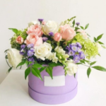 An assortment of pink roses, white roses & green hydrangeas in a purple round box
