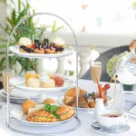 High tea for 2, short eats and snacks laind out on a tower tray with tea being poured into a cup. Location is the verhandah restaurant at the galle face hotel in colombo sri lanka.