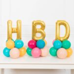 This arrangement features three letter balloons (not helium) and latex balloons. The balloon color theme and numbers can be customized to your preference. Foil letters are available in gold, silver, and rose gold, and they are 16” in size.