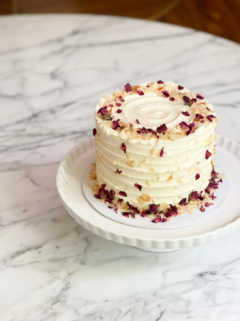 Enjoy a delightful 1.2kg Ribbon Almond Cake, adorned with toasted almonds and delicate rose petals—a perfect blend of flavor and elegance The cake has dimensions of 6 inches in diameter and 4-5 inches in height