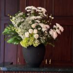 Gift a sophisticated arrangement of white roses, lush hydrangeas, delicate chrysanthemums, and elegant orchids, accented with fresh foliage in a sleek black vase. A timeless expression of beauty and grace for any occasion.