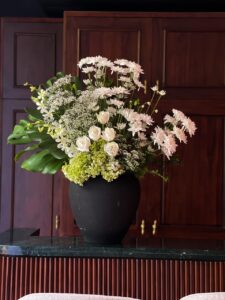 Gift a sophisticated arrangement of white roses, lush hydrangeas, delicate chrysanthemums, and elegant orchids, accented with fresh foliage in a sleek black vase. A timeless expression of beauty and grace for any occasion.